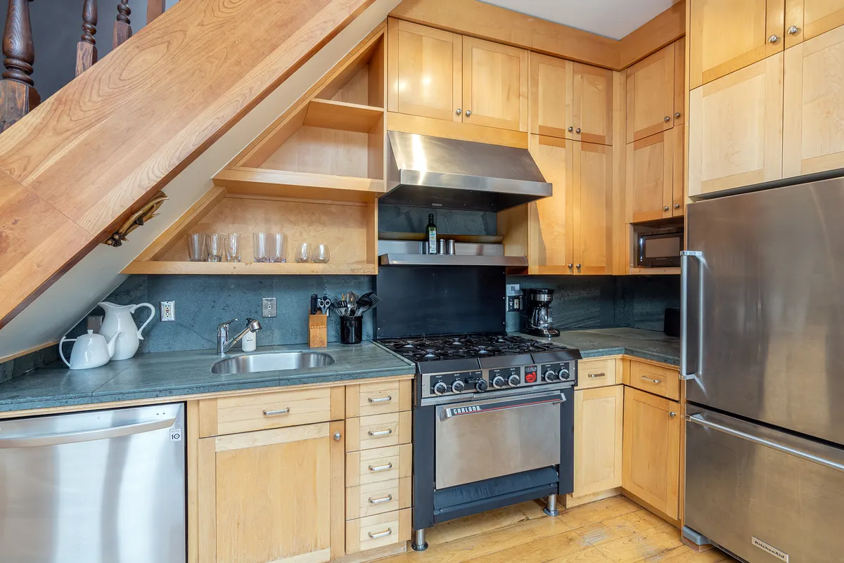 A modern kitchen featuring gleaming stainless steel oven, wooden cabinetry, granite countertops, and a well-lit sink area. The space is bustling with meal preparation, evoking a sense of warmth and efficiency.