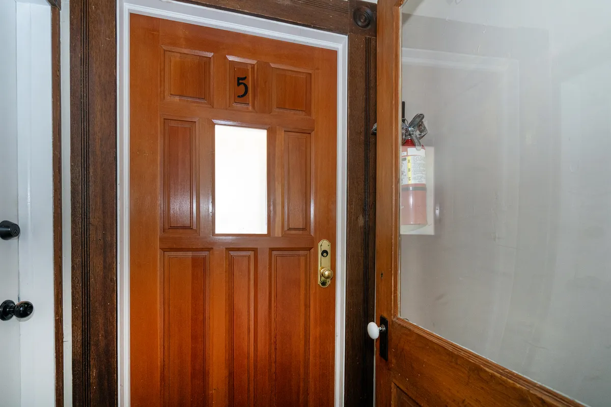 This image features the front door, clearly marked with 'door number 5', accompanied by a fire extinguisher nearby. The ambiance is welcoming, emphasizing the moment of arrival and the transition from the outside world into the home. The focus on the entry point aligns with the concept of launching adventures and creating first impressions.