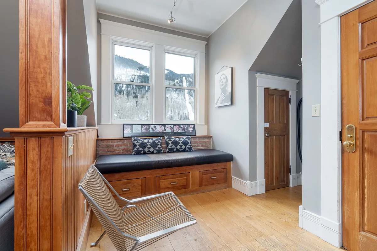 A sunlit interior space with large windows framing stunning mountain views, wooden bench seating, and decorative wall art, creating a warm, inviting setting for relaxation or gathering with friends between festival events.