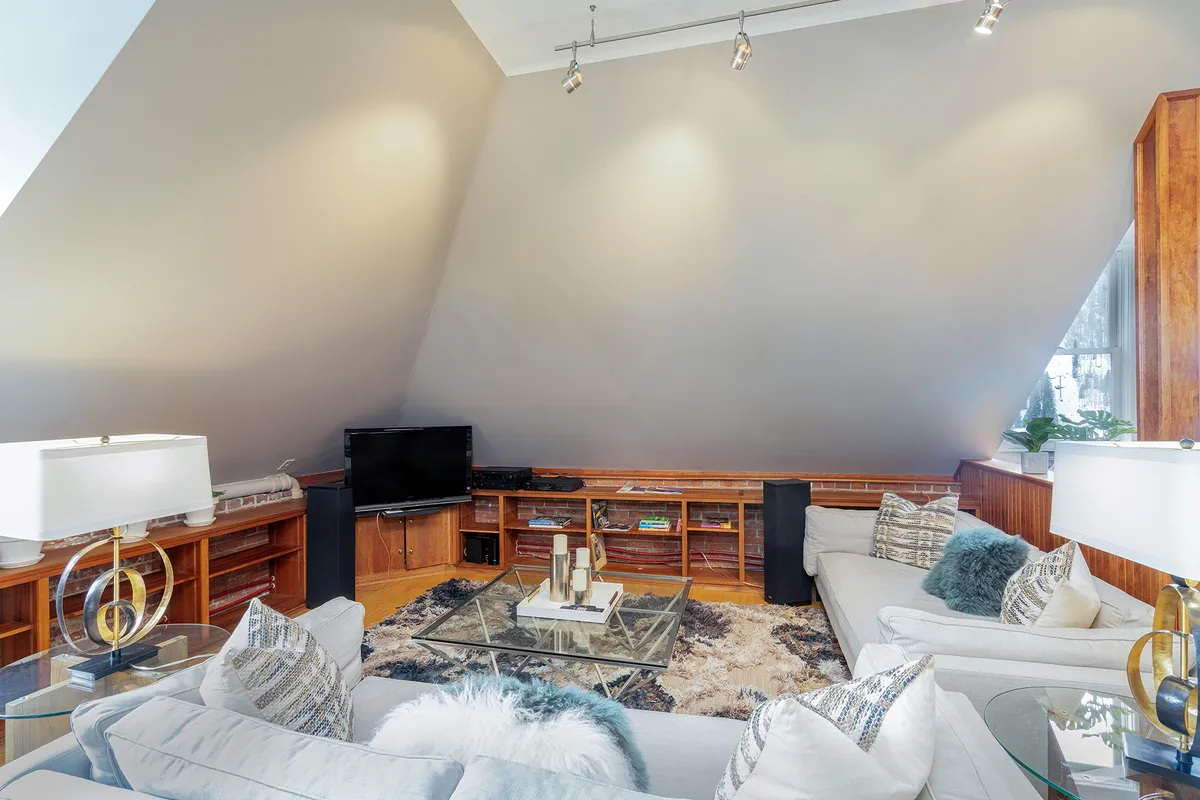 A comfortable living area featuring a plush sofa, coffee table, entertainment unit with a smart TV, and a standing lamp. The space is brightened by natural light and is arranged for both relaxation and socializing, ideal for movie nights or intimate gatherings.